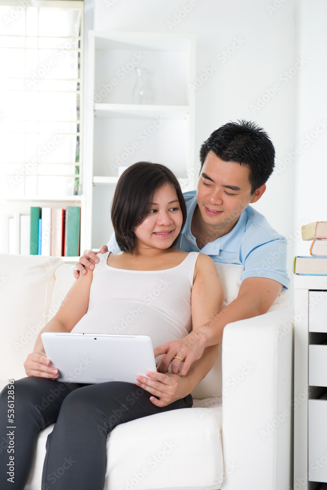 Asian couple. Husband and 8 months pregnant wife using tablet co Asian couple. Husband and 8 months pregnant wife using tablet co
