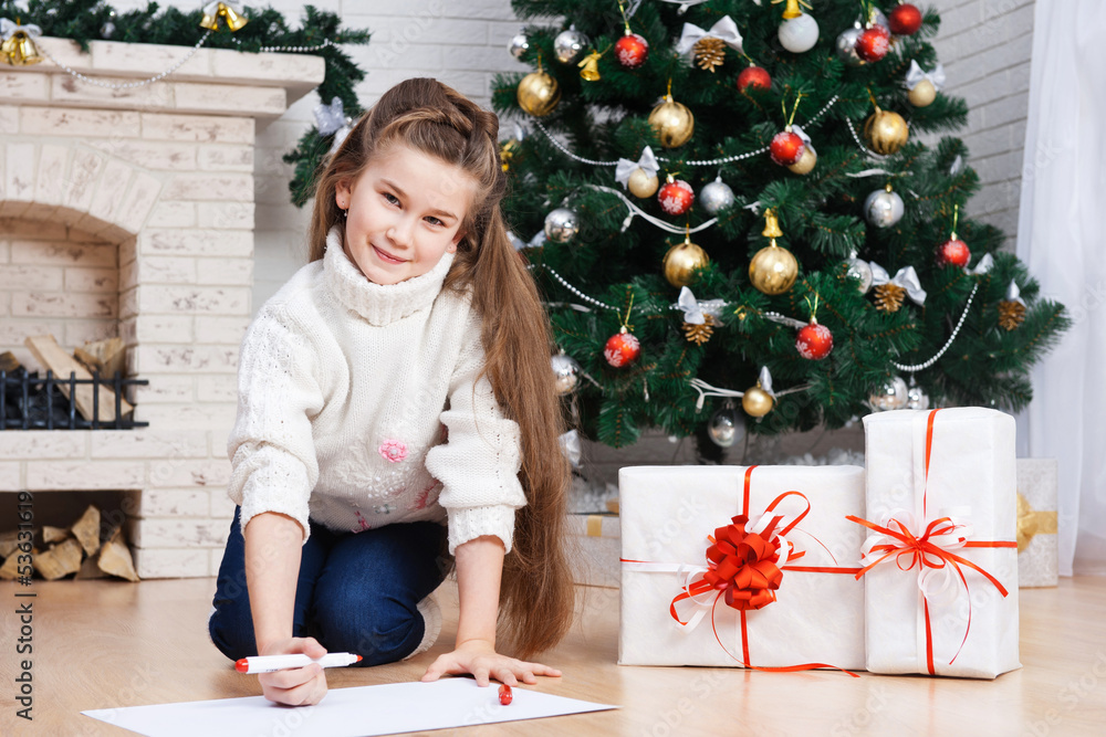 Little girl writes letter to Santa near christmas tree