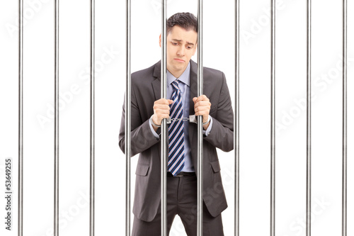 Tablou canvas Handcuffed businessman in suit posing in jail and holding bars