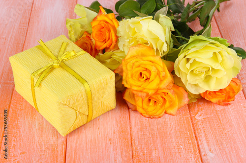 Beautiful bouquet of roses with gift on table close-up