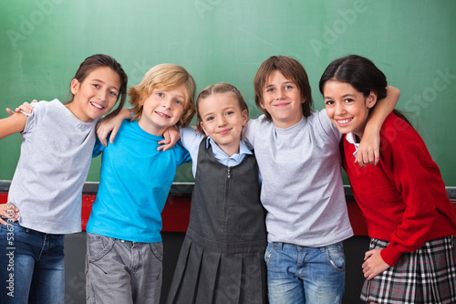 Cute Schoolchildren With Arms Around Standing Together In Classr