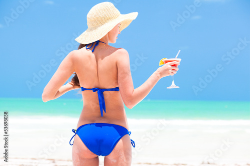 Happy young woman in straw hat with cocktail on the beach