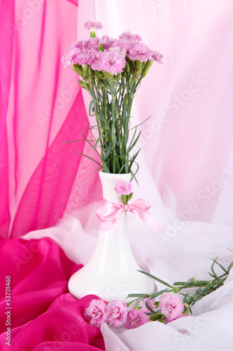 Many small pink cloves in vase on light fabric background