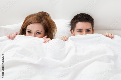 Portrait of young couple hiding face with blanket