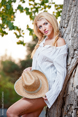 blond woman sitting down outdoor on the yellow grass with a hat