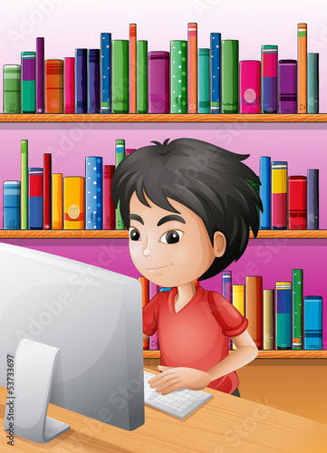 A boy playing computer in front of the shelves with books
