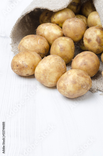 new potatoes in a sack on white wooden board and space for text