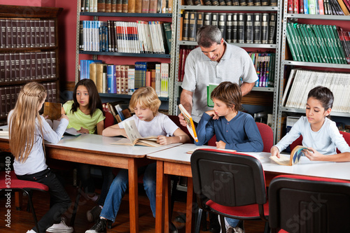 Teacher Showing Book To Schoolboy In Library