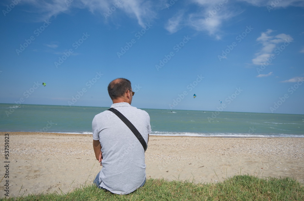 man on the beach watching at kite surfers