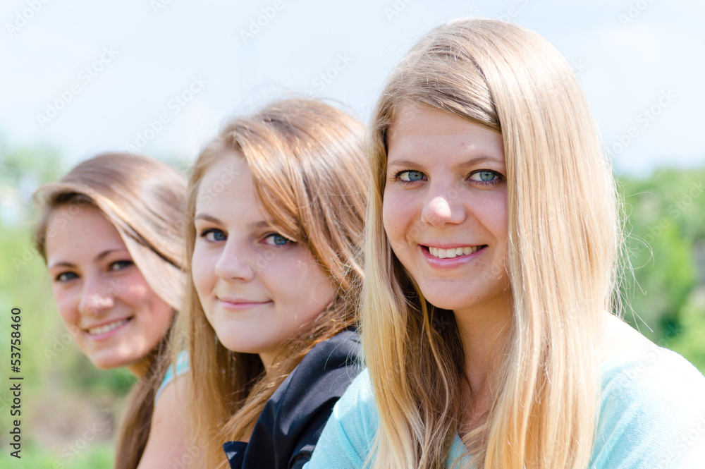 Obraz premium Three happy teen girls looking down against blue sky