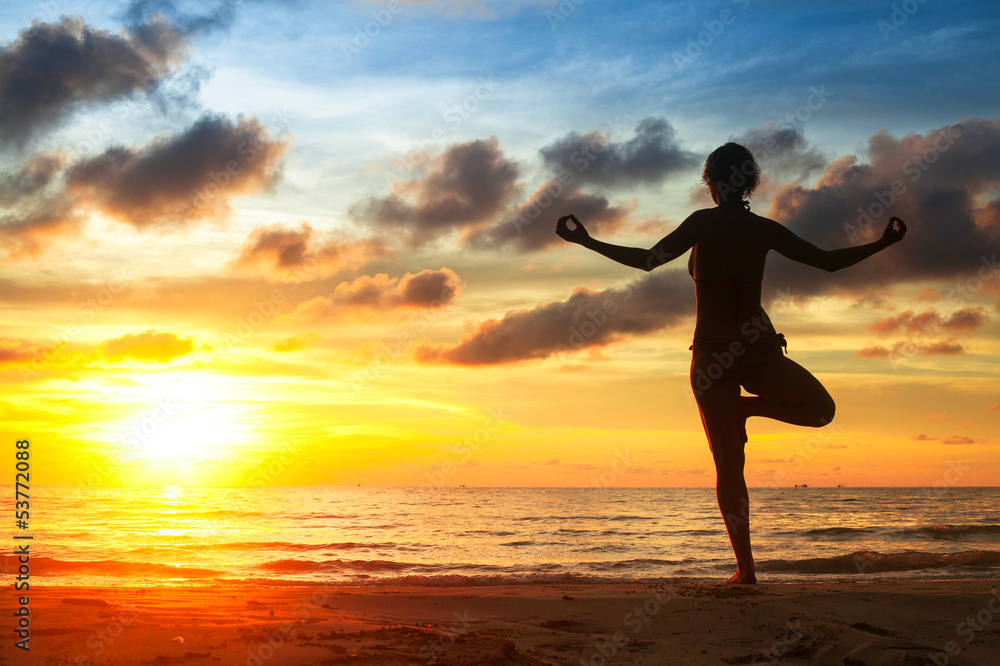 Woman practicing yoga on the beach, during sunset.