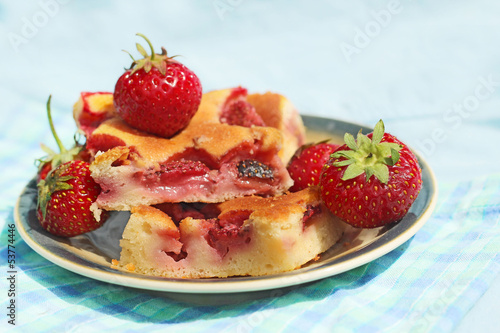 A piece of cake with strawberries on plate on blue background