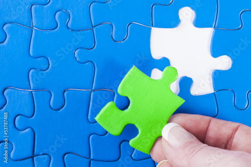 Woman's hand placing missing piece in Jigsaw puzzle  signifying