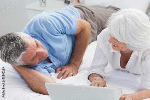 Couple lying in bed and using a laptop