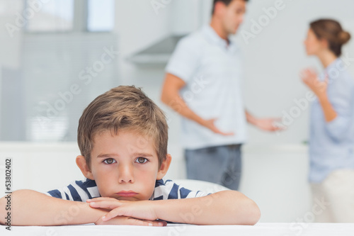 Sad boy with arms folded while parents quarreling