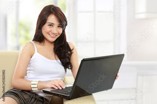 young asian woman sitting in sofa using a laptop © Odua Images