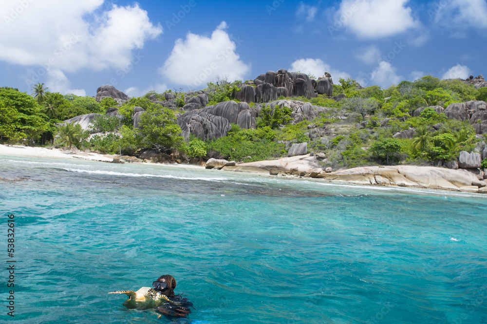 A snorkeler at an island coral reef with turtle. Seychelles.