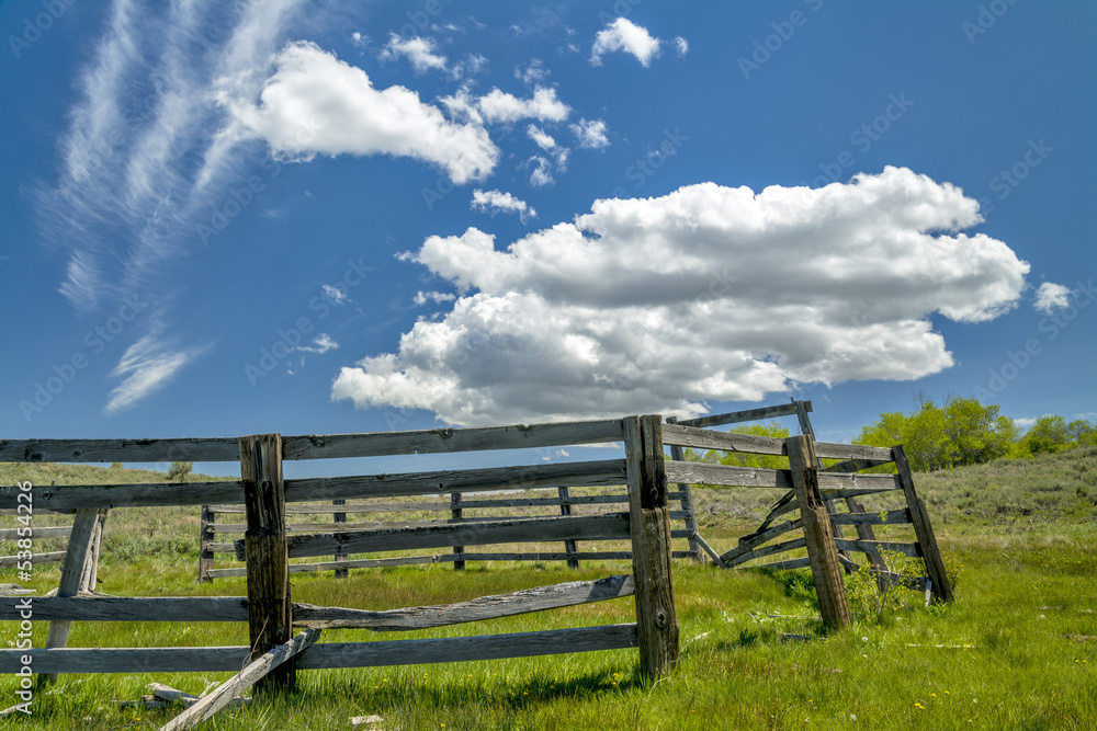 Broken down corral in a field with clouds