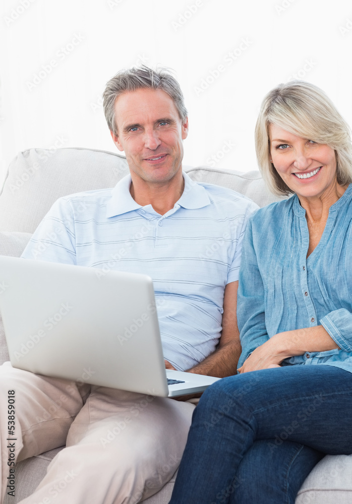 Couple using laptop together on the couch smiling at camera Couple using laptop together on the couch smiling at camera