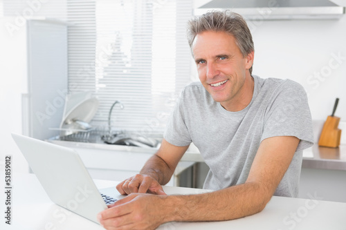 Cheerful man using laptop in kitchen