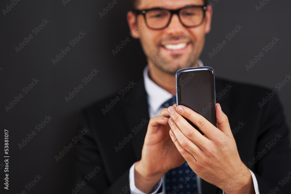 Smiling businessman text messaging on smart phone . Smiling businessman text messaging on smart phone .