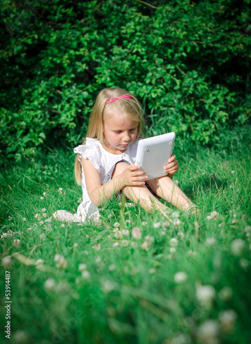 Little girl sitting with computer outdoors.