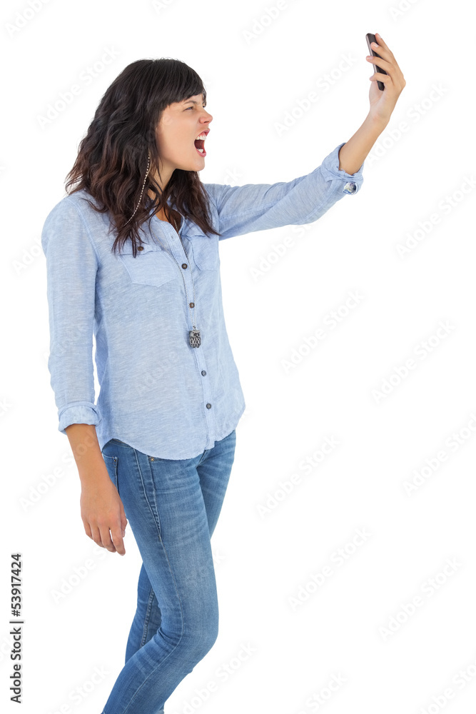 Furious brunette holding her mobile phone and screaming