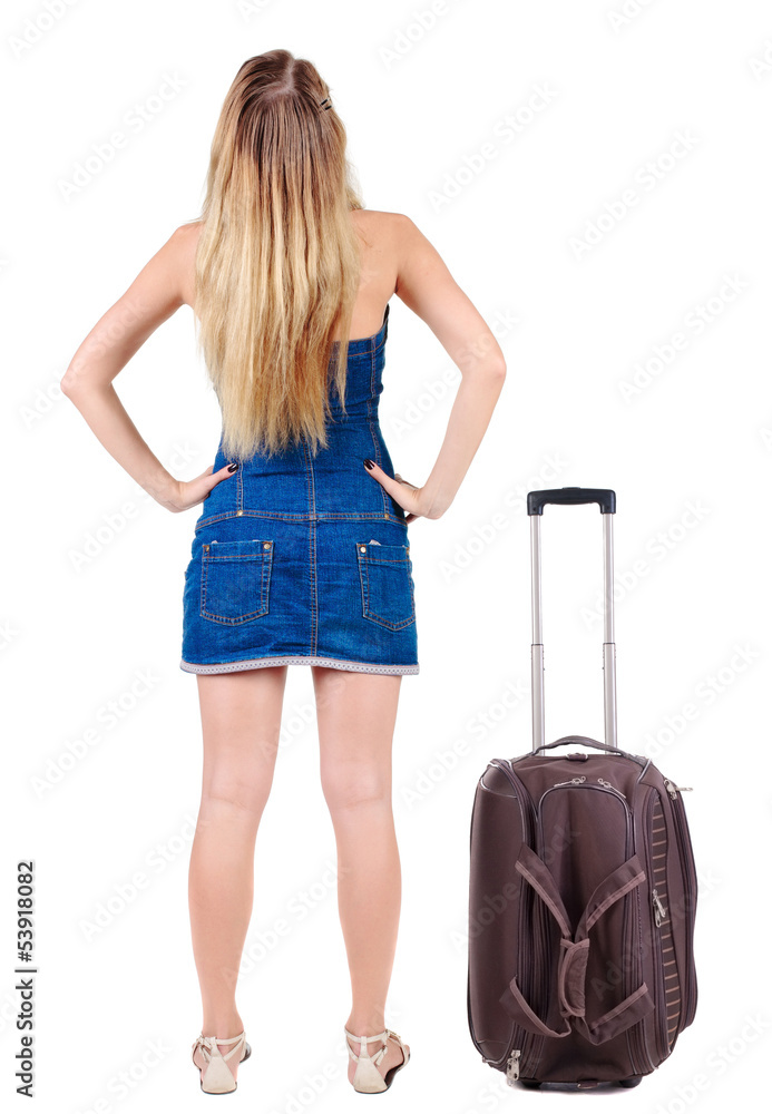 Back view of traveling blonde woman in dress with suitcase looki Back view of traveling blonde woman in dress with suitcase looki