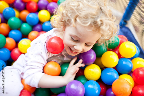 A young blond girl child having fun playing with сolorful balls