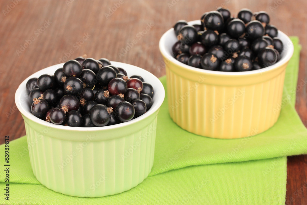 Fresh black currant in bowls on napkin on wooden background Fresh black currant in bowls on napkin on wooden background