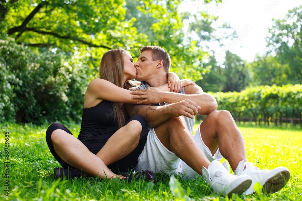 Young happy smiling sporty couple sitting on a meadow Young happy smiling sporty couple sitting on a meadow