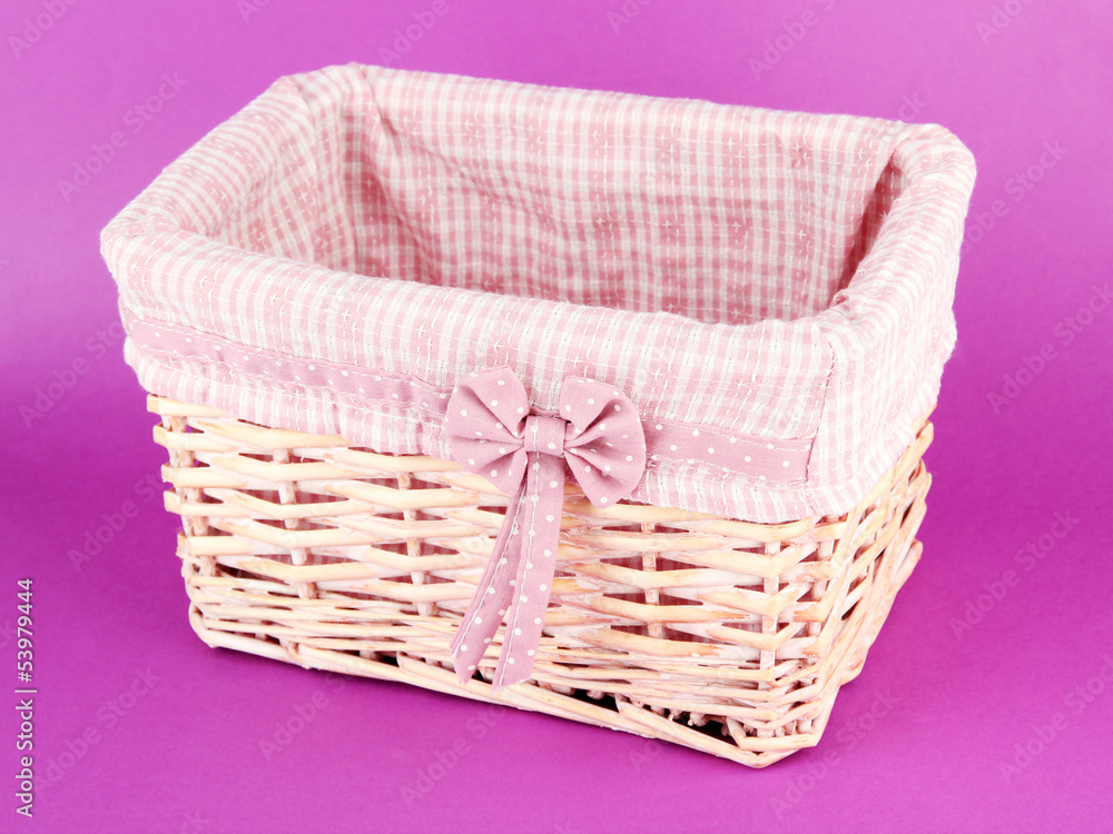 Wicket basket with pink fabric and bow, on color background Wicket basket with pink fabric and bow, on color background