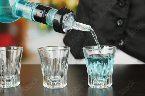 Barmen hand with bottle  pouring beverage into glasses,