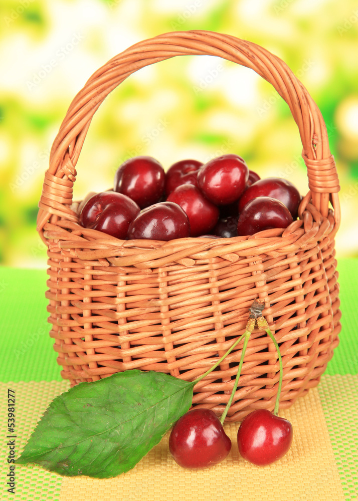 Cherry berries in wicker basket on table on bright background Cherry berries in wicker basket on table on bright background