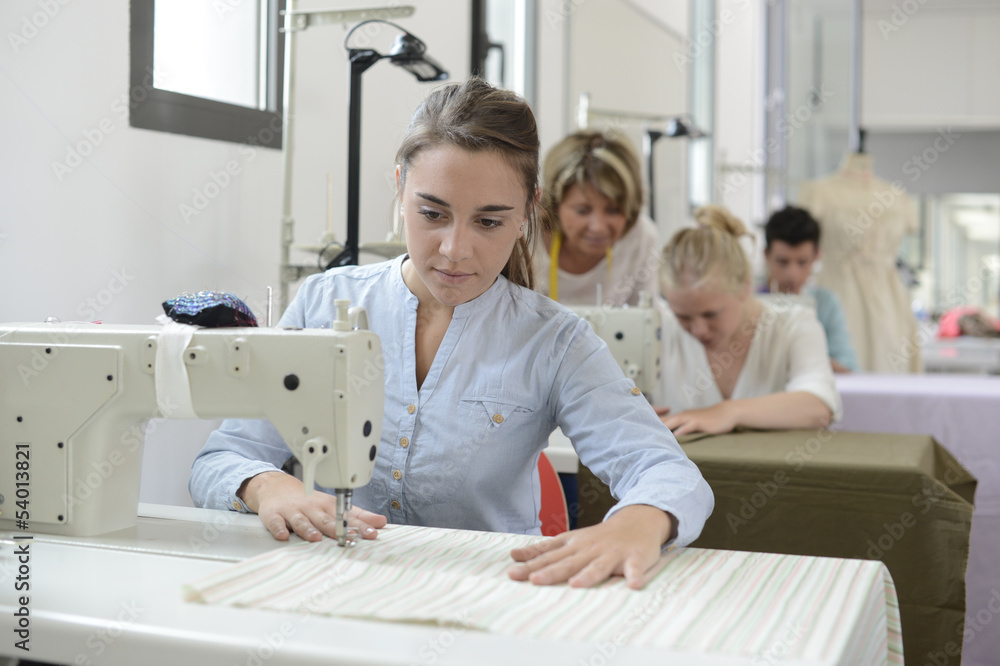 Student girl in training class working on sewing machine Student girl in training class working on sewing machine