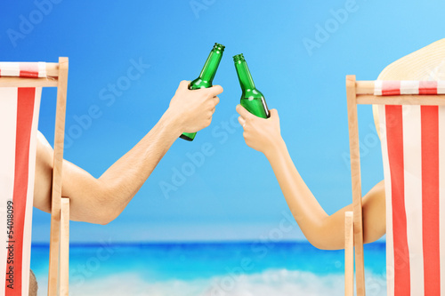 Man and woman relaxing on a beach and cheering with beer