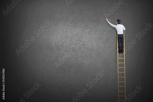 businessman standing on ladder drawing diagrams and graphs photo