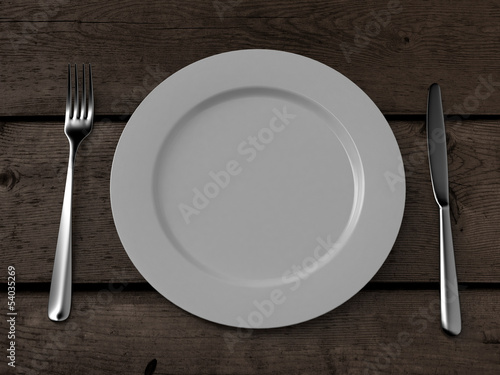 white plate, knife and fork on wooden table