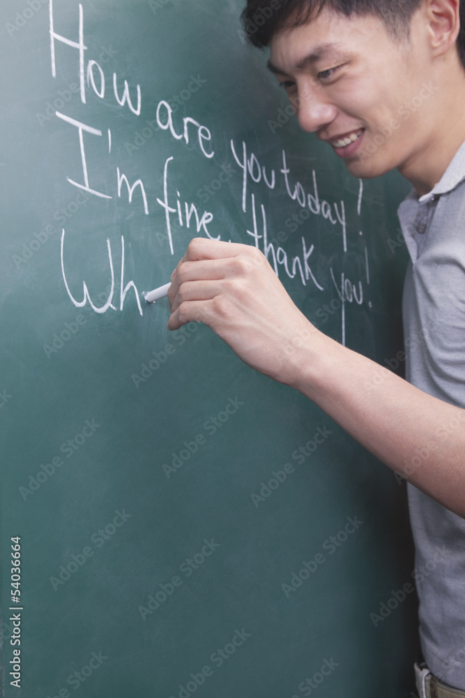 Young man writing English sentences on the blackboard