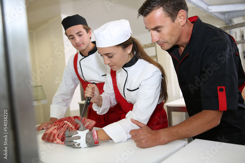 Professional butcher teaching students with meat cutting photo