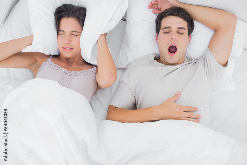 Woman covering ears with a pillow while her partner is snoring Woman covering ears with a pillow while her partner is snoring