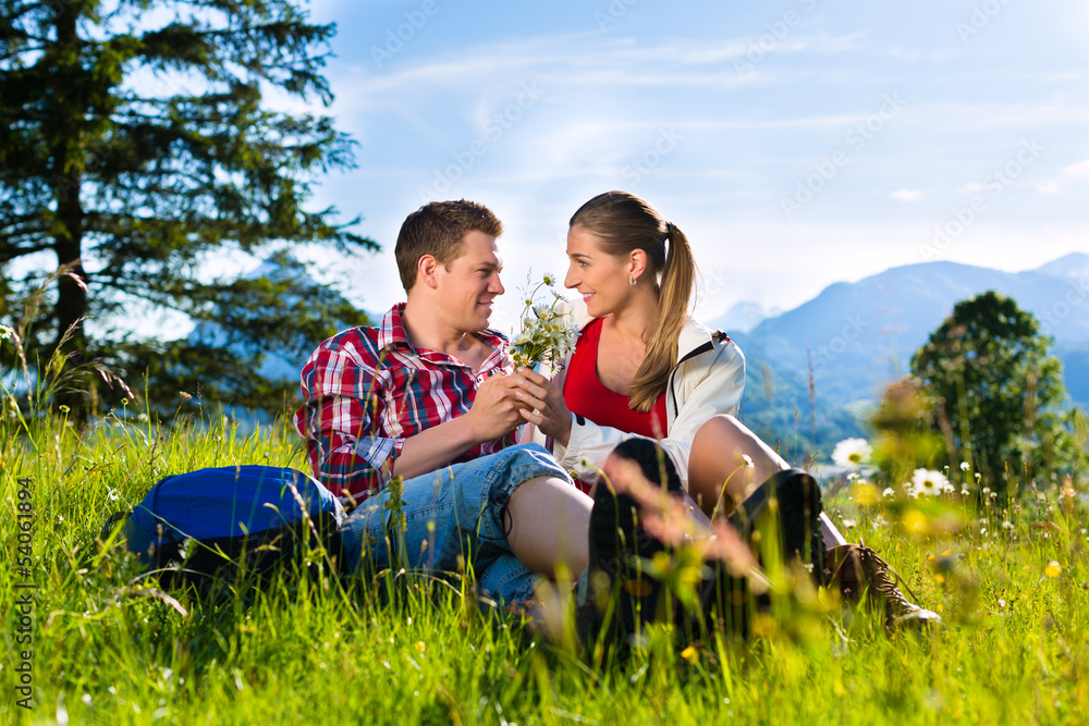 Fototapeta premium Glückliches Paar sitzt in auf Wiese vor Bergpanorama