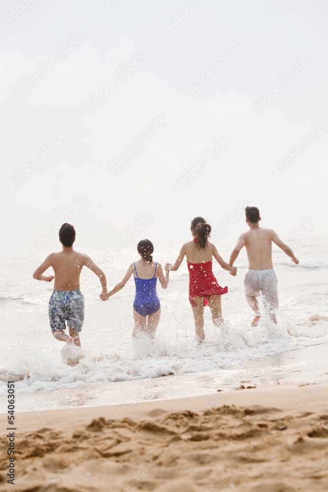 Four friends running into the water on a sandy beach, rear view