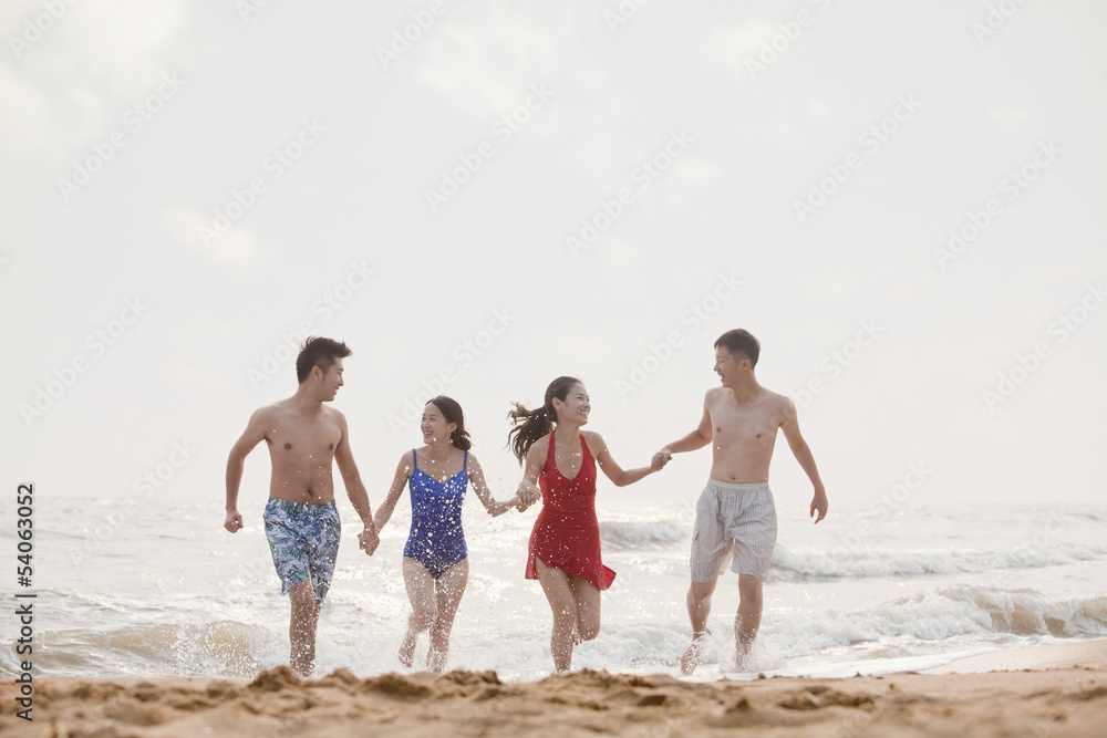 Four friends running out of the water on a sandy beach