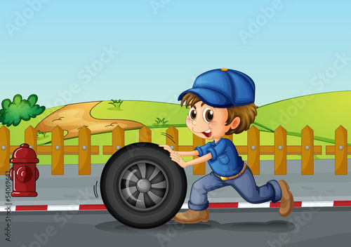 A boy wearing a hat pushing a wheel along the road