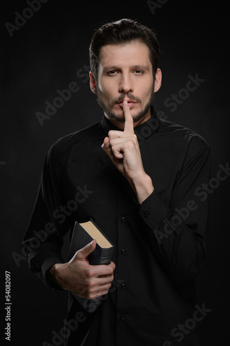 Asking to keep silence. Portrait of priest holding his hand agai