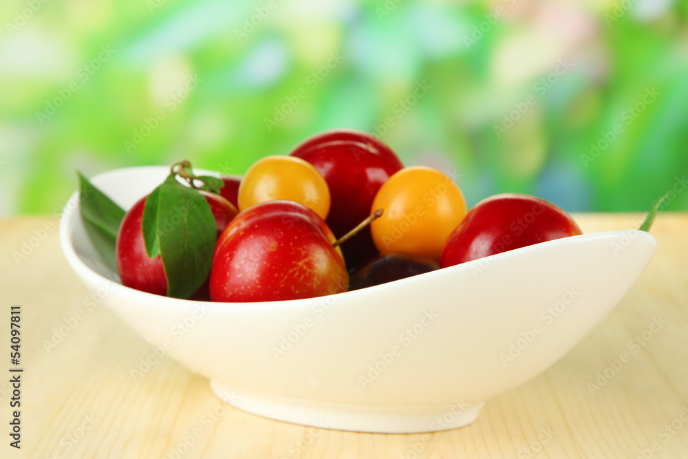 Ripe plums in plate on wooden table on natural background Ripe plums in plate on wooden table on natural background