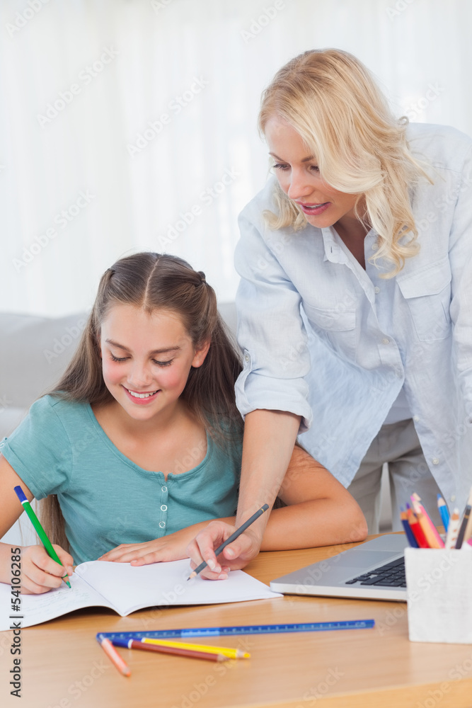 Little girl writing on a book while her mother is helping her Little girl writing on a book while her mother is helping her