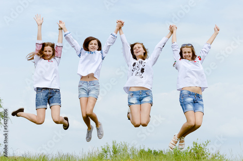 Four happy teenage friends jumping high in blue sky