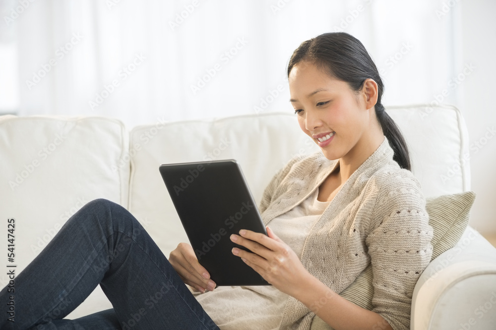 Beautiful Woman Using Digital Tablet While Relaxing On Sofa Beautiful Woman Using Digital Tablet While Relaxing On Sofa
